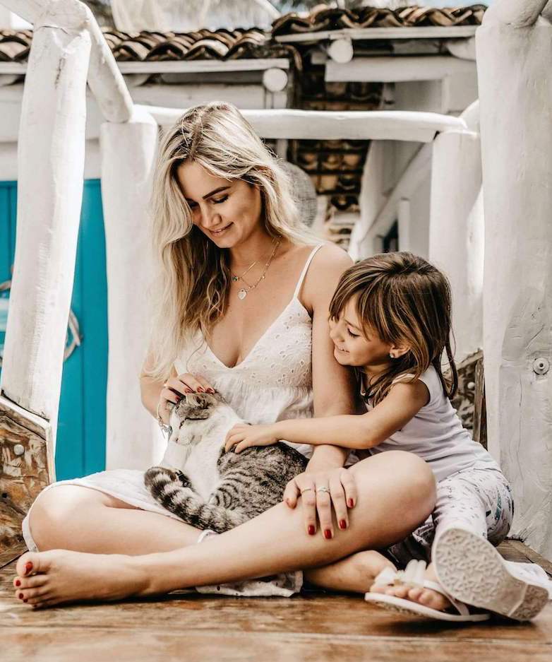 Woman holds gray and white tabby cat while young child pets cat
